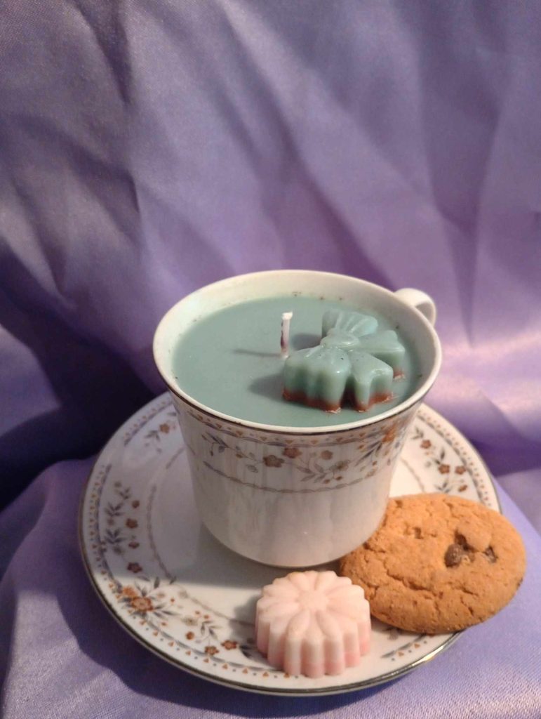 a picture of a candle built in a tea cup with a cookie beside it